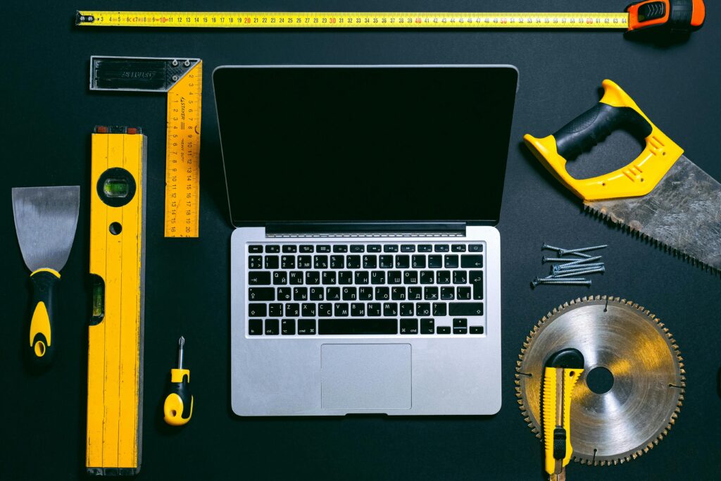 pexels photo 4312861 4312861 Overhead view of a laptop surrounded by various hand tools on a dark background, representing technology and construction.